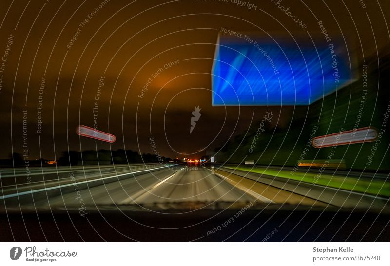 Die lang belichtete Aufnahme einer nächtlichen Autobahnfahrt bei schneller Fahrt über eine deutsche Autobahn und ein typisches blaues Schild. Licht Gebäude