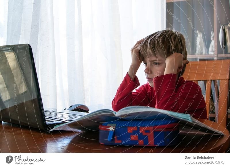 Schulkind in Selbstisolation mit Laptop für Hausaufgaben, Sozialer Fernunterricht im Online-Unterricht während der Coronavirus-Epidemie. Süßer Junge lernt und macht zu Hause während der Quarantäne seine Hausaufgaben