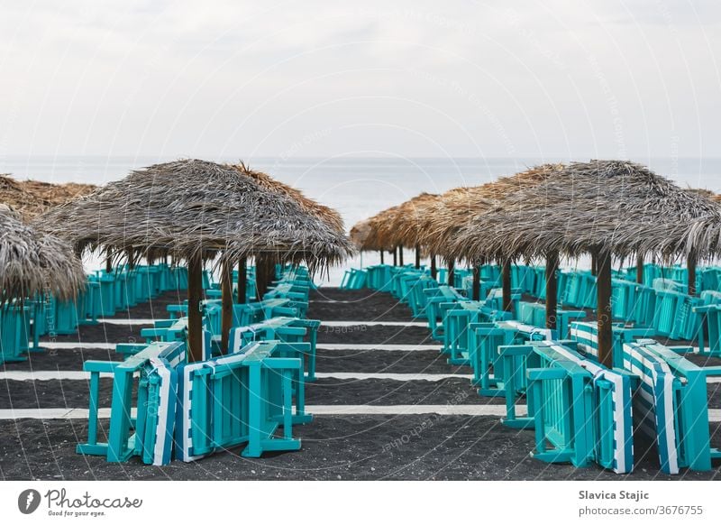 Sonnenbänke und Sonnenschirme auf blankem Sandstrand. Perissa, Insel Santorin, Griechenland ägäisch Strand Strandpromenade schwarz blau Caldera Küste