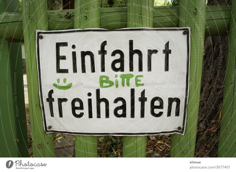 "Einfahrt BITTE freihalten" steht auf einem zerbeulten Metallschild an einem grünen Holzlattenzaun Einfahrt freihalten Bitte Schild Wunsch Zaun Holzzaun Smiley