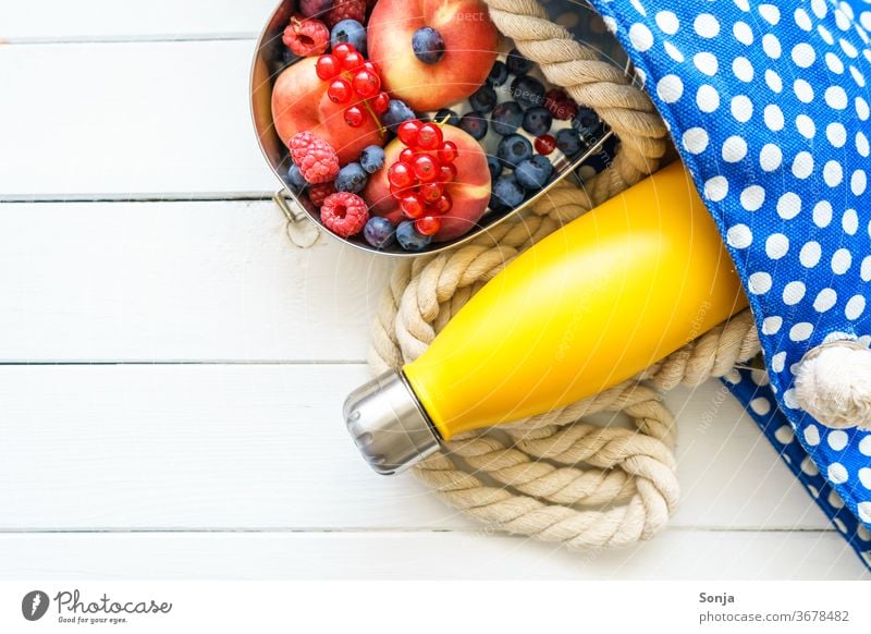 Strandtasche mit einer gelben Wasserflasche und frisches Obst in einer Blechdose. Draufsicht. Badetasche strandurlaub Urlaub Meer Reise Sommerurlaub Farbfoto