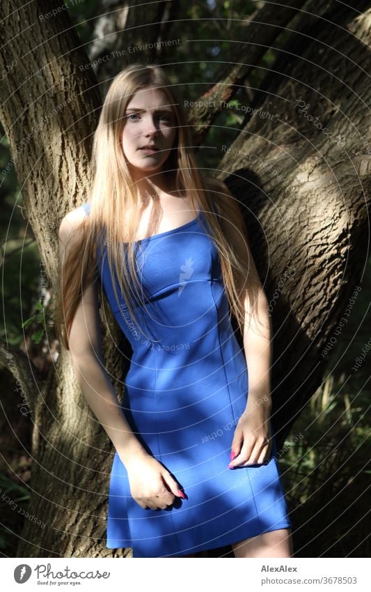 Portrait einer jungen Frau in blauem Sommerkleid vor einem Baum mit Schattenspiel Reinheit Glück Schönes Wetter Ausflug Erwartung Sonnenlicht Nahaufnahme Tag