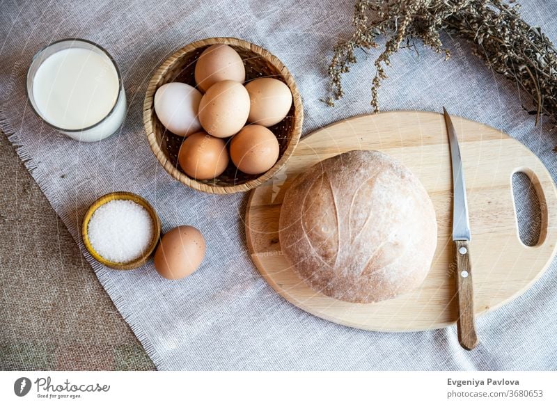 Ein Laib frisches, selbstgebackenes Brot, Milch, Eier und Salz auf einem Holzteller. Stilleben im rustikalen Stil, Ansicht von oben. Teigwaren Gebäck