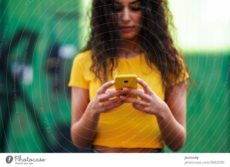 Junge arabische Frau geht auf der Straße mit ihrem Smartphone jung Texten Nachricht Nahaufnahme Tippen gelb copyspace Mädchen Aufnahme Frisur attraktiv schön