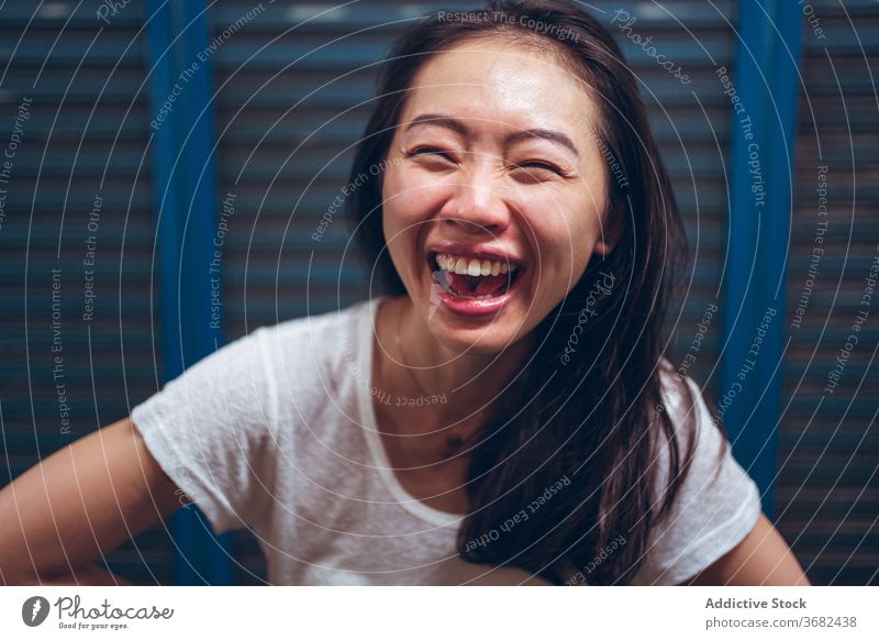 Fröhliche junge ethnische Frau, die in die Kamera lacht heiter Lachen Glück Freude Spaß haben aufgeregt positiv Porträt asiatisch froh lässig Optimist modern