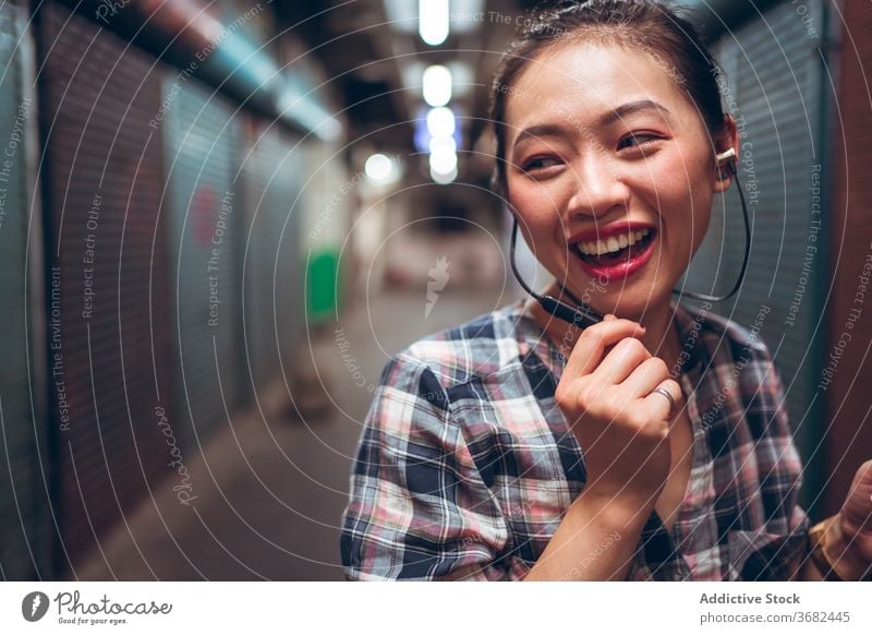 Fröhliche Frau mit Headset in der Stadt Glück heiter Kommunizieren Lachen reden jung lässig urban asiatisch ethnisch tausendjährig Freude Gespräch Lifestyle