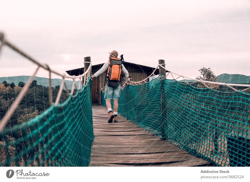 Anonymer Reisender, der über einen Holzsteg geht Suspension Steg Tourist Mann Spaziergang Rucksack bewundern Landschaft hölzern Urlaub männlich Abenteuer