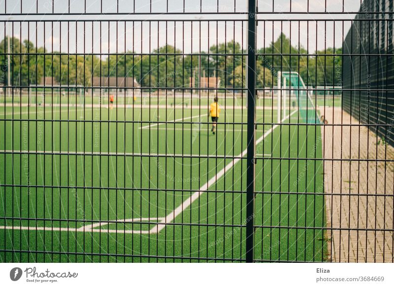 Junger Fussballer auf einem Fußballfeld hinter einem Zaun Fussballfeld Fußballplatz Sport Spielen Sportplatz Ballsport Freizeit & Hobby Gitter Sportstätten Tor