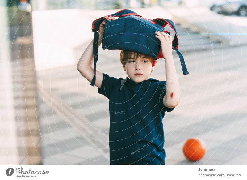 Ein müder Junge in Sportuniform und mit einer Wunde am Arm kehrt nach dem Basketballtraining nach Hause zurück. Bildung, Erziehung, Sportunterricht Rucksack