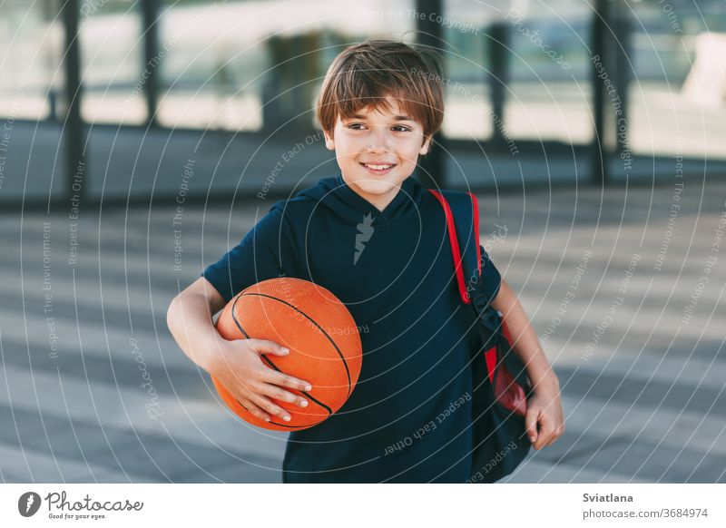 Porträt eines schönen Jungen in Sportuniform mit Rucksack und Basketball. Der Junge lächelt und hält den Ball in seinen Händen. Training, Erziehung, Sportunterricht