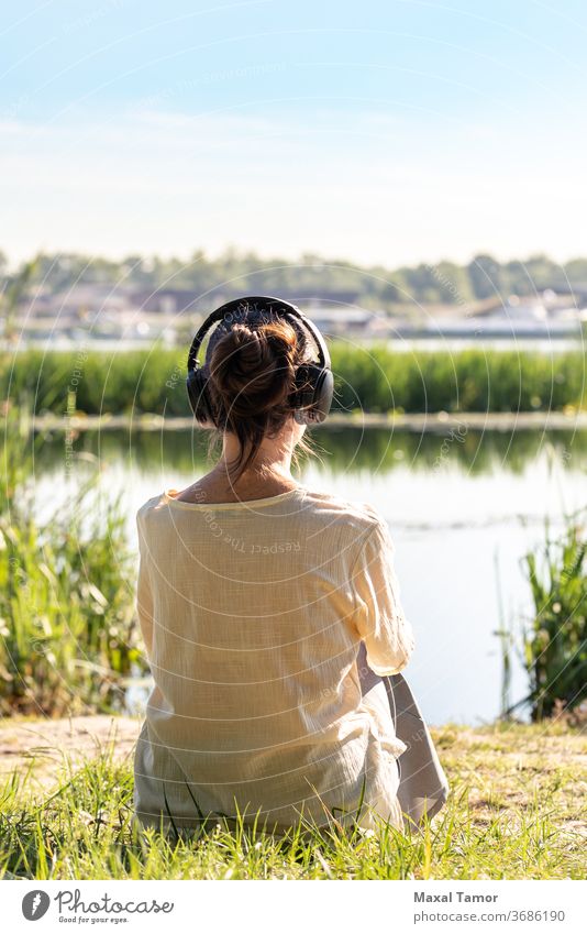 Frau mit Kopfhörern meditiert, sie sitzt vor dem Fluss, kurz nach Sonnenaufgang. Erwachsener schön Schönheit Körper Windstille Kaukasier Konzentration Energie