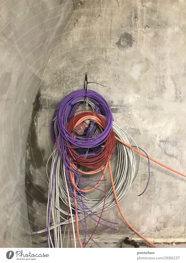 Bunte Kabel hängen aufgerollt an einer Betonwand . Kabelsalat baustelle kabelsalat leitungen rollen lila bunt Technik & Technologie Energiewirtschaft