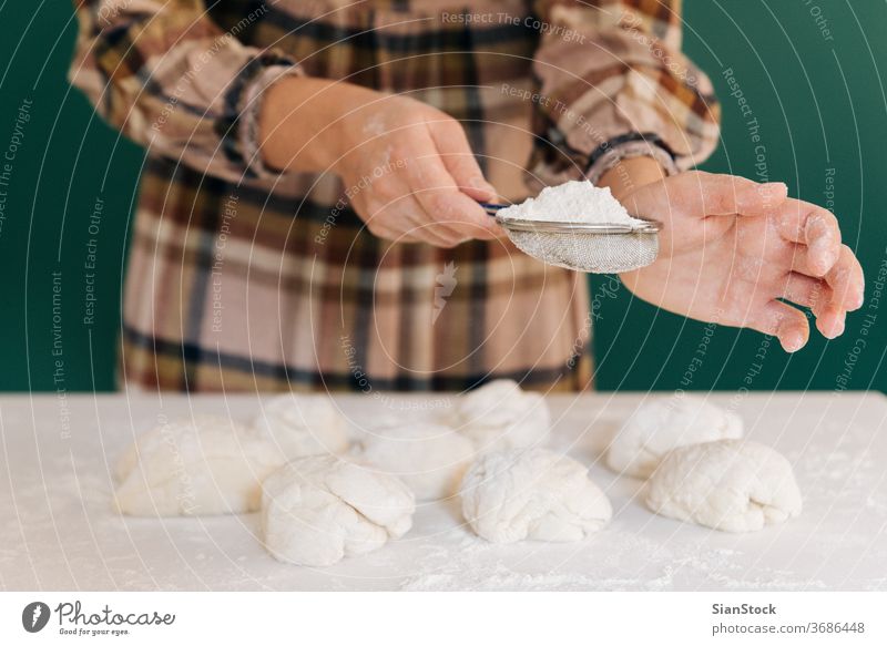 Frau streut Mehl zu handgemachten Teigstücken für Brot, hausgemachtes Kochen. Teigwaren handgefertigt Streusel Hände Essen zubereiten weiß Person Pulver