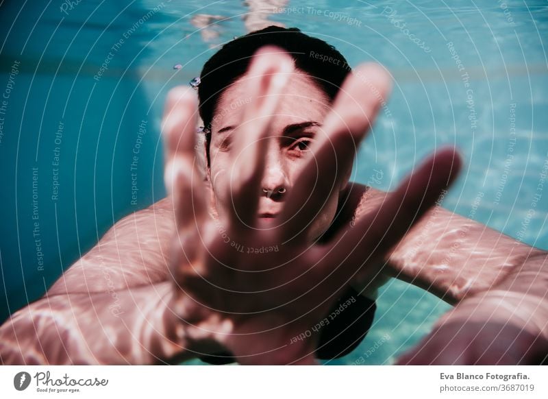 Porträt einer jungen Frau, die in einem Schwimmbad unter Wasser taucht. Sommer und lustiger Lebensstil berührend Hand Schwimmsport Blasen Spaß Kaukasier Pool