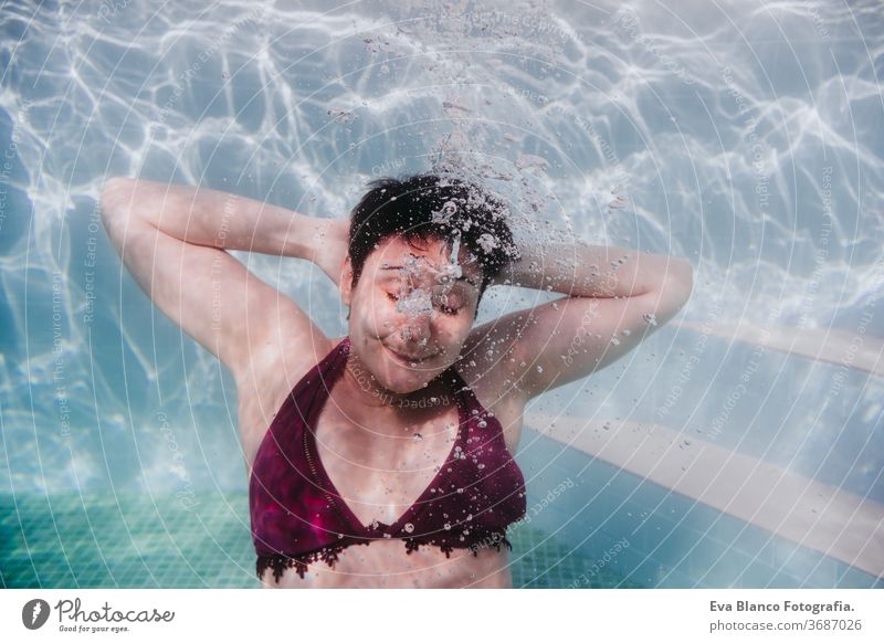 junge Frau, die in einem Schwimmbad unter Wasser taucht. Arme hinter dem Kopf ruhen. sommerlicher und lustiger Lebensstil Porträt abschließen Schwimmsport