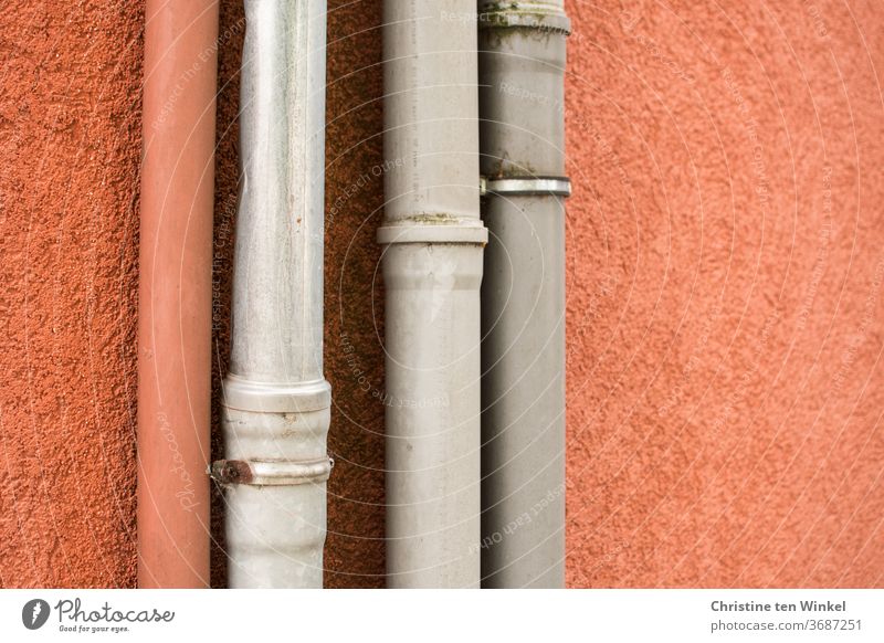 Fallrohre vor einer orange verputzten Wand, ein orangefarbenes und drei graue Fassade Haus Strukturen & Formen Detailaufnahme Putz Gebäude Abwasser
