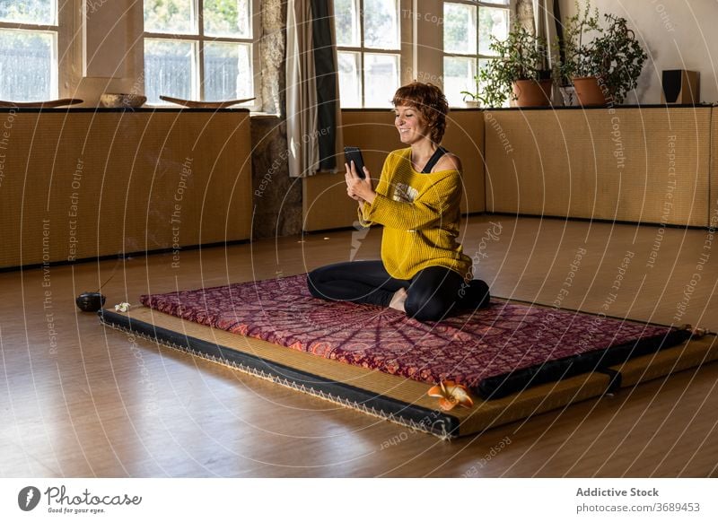 Lächelnde Frau mit Smartphone und macht Yoga üben benutzend sich[Akk] entspannen Browsen Atelier Unterlage beweglich Apparatur Gerät online Wohlbefinden