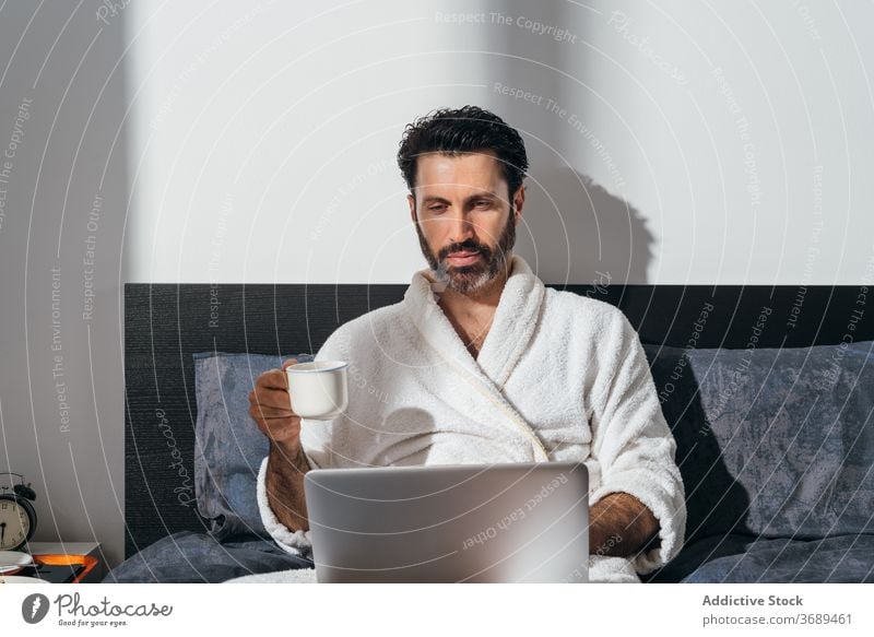 Ruhiger Mann beim Frühstück im Bett freiberuflich Kaffee Laptop Arbeit abgelegen Bademantel benutzend männlich Geschäftsmann Tasse frisch Morgen trinken Gerät