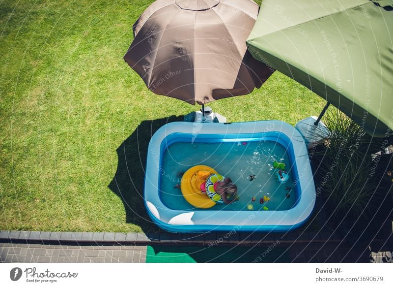 Kind badet im Garten in einem Planschbecken umringt von Sonnenschirmen die Schatten spenden schattenspender Sonnig Quarantäne Eigenheim Kindheit Mädchen baden