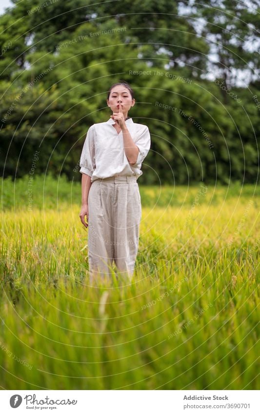 Ethnische Frau zeigt Schweigegebärde im Feld stumm gestikulieren Ruhe Lippe Reis Natur Zeichen Windstille asiatisch ethnisch zeigen geheim shh charmant stehen