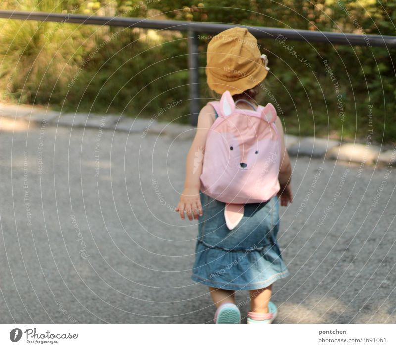 Ein Kleinkind mit einem gelben Sonnenhut und einem süßen Rucksack in rosa. Familienausflug, Familienurlaub rucksack urlsub reise kleidung sommer selbstbewusst
