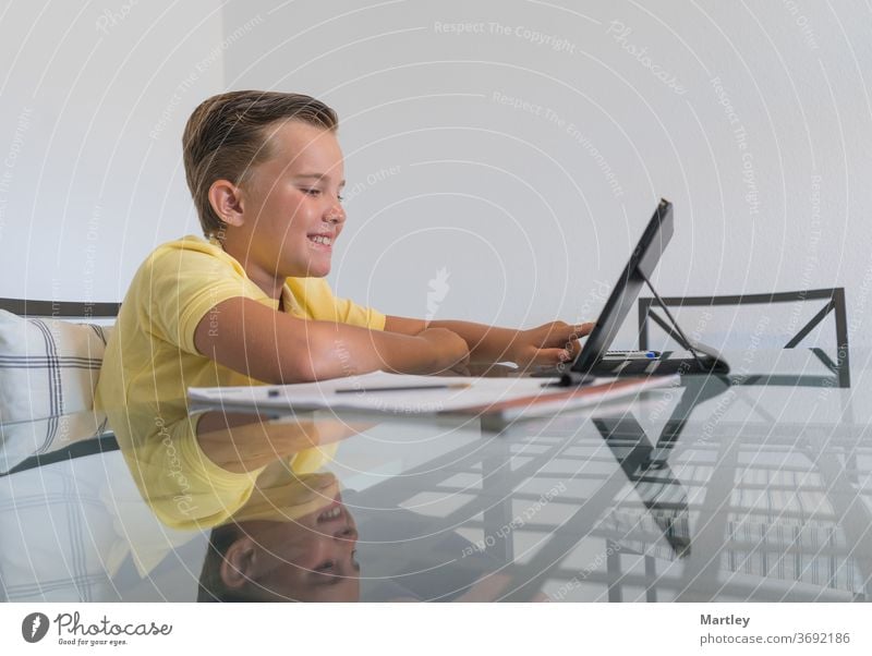 Junge spricht mit einem Klassenkameraden während einer Videokonferenz auf einem Tablet und diskutiert Hausaufgaben, während er in einem modernen, hellen Raum am Tisch sitzt.