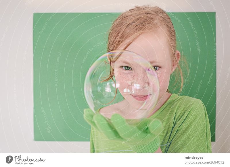 Mädchen in Grün schaut frech durch eine Seifenblase Seifenblasen grün Magie Handschuhe Spielen spass Kindheit Freude lustig Sommersprossen Farbfoto portraitfoto