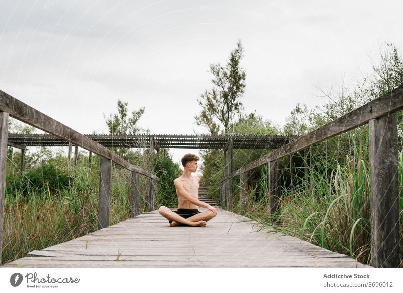 Shirtless Mann macht Yoga auf der Terrasse padmasana üben beweglich Natur Windstille männlich Pose Harmonie Konzentration Zen Asana hölzern Gesundheit