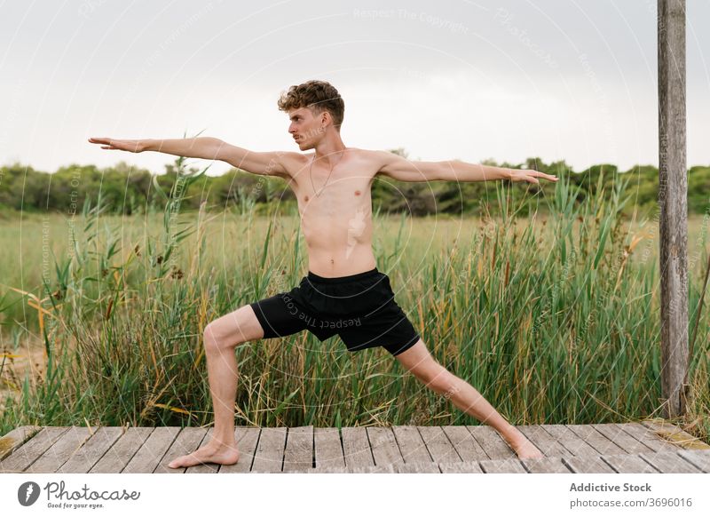 Flexible Mann tun Yoga in Krieger zwei Pose üben beweglich friedlich Harmonie Natur Terrasse männlich Gesundheit ruhig Gleichgewicht Körper Vitalität Wellness