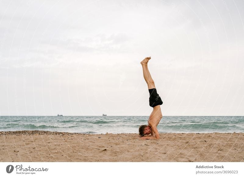 Junger Mann in Unterarm Balance Yoga-Pose am Strand üben Sand Asana Unterarmstativ Pincha Mayurasana fortgeschritten Gleichgewicht Umkehrung männlich jung Yogi