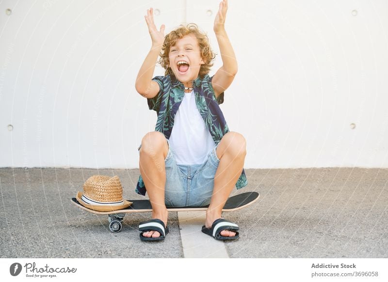 Kind in Sommerkleidung sitzt auf einem Skateboard und gestikuliert freudig dynamisch extrem Fähigkeit Vitalität Skater Skateboarderin Jugendzeit Gleichgewicht