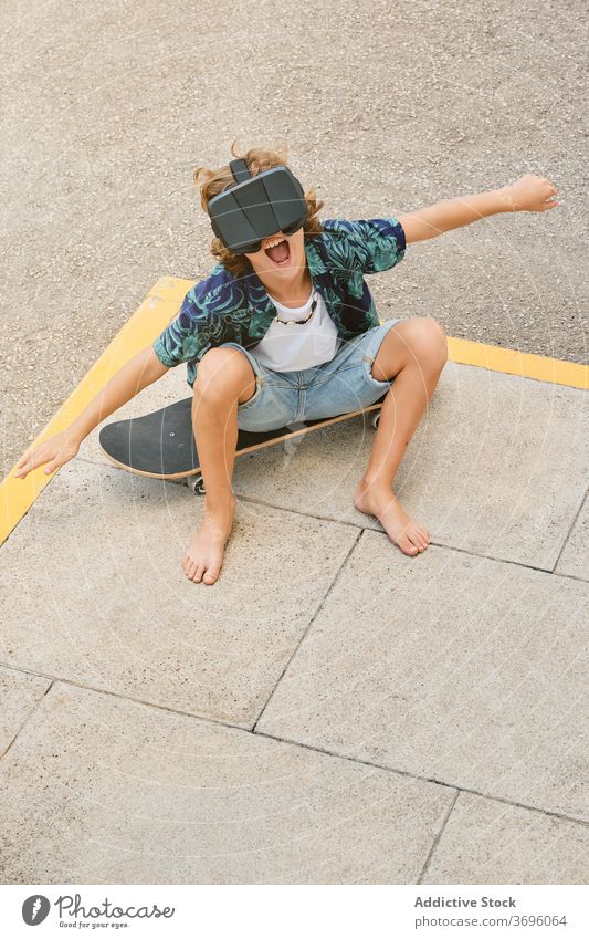 Junge sitzt auf einem Skateboard, trägt eine Virtual-Reality-Brille und gestikuliert, während er fliegt vertikal Reaktionen u. Effekte berührend gestikulierend