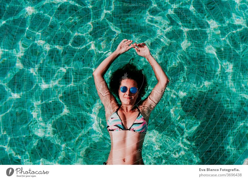Draufsicht auf eine glückliche junge Frau, die in einem Pool schwebt. Sommer und lustiger Lebensstil unter Wasser Schwimmsport Blasen Spaß Kaukasier Sinkflug