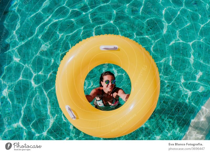 Draufsicht einer glücklichen jungen Frau in einem Pool mit einem gelben Donut in der Hand. Sommer und lustiger Lebensstil gelbe Donuts aufblasbar Schwimmsport