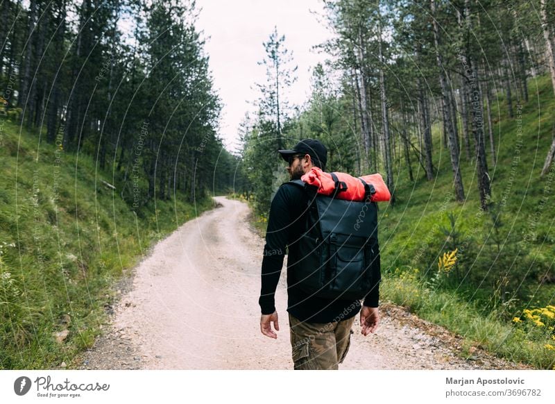 Junger männlicher Naturforscher geht auf dem Feldweg durch den Wald aktiv Abenteuer Rucksack Backpacker Rucksacktourismus Landschaft Schmutz erkunden Entdecker