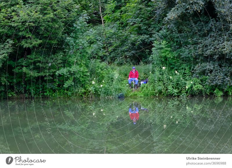 Angler sitzt am Flussufer im Grünen Angeln Wasser Fischer Ansitzen Ufer Gebüsch Wald grün Geheimplatz Erholung Stille Ruhe Fische fangen Freizeit & Hobby Natur