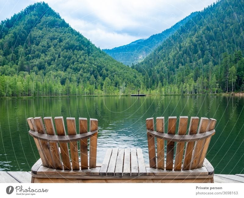 Zwei leere Holzliegenstühle am Strand, schöne Landschaft mit Bergsee, Urlaub in den Bergen, luxuriöses Sommerferienkonzept. See Natur Windstille reisen Himmel