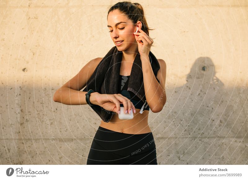 Sportliche Frau mit Kopfhörern und Fitness-Tracker ruht in der Nähe der Wand Sportlerin prüfen Armband App passen schlank Straße Training benutzend Gerät aktiv