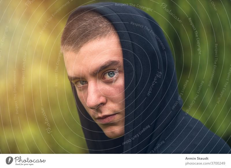 Porträt eines ernsthaften jungen Mannes in einem schwarzen Kapuzenpulli Aussehen Teenager Blick männlich schön lässig Kaukasier im Freien selbstbewusst Model