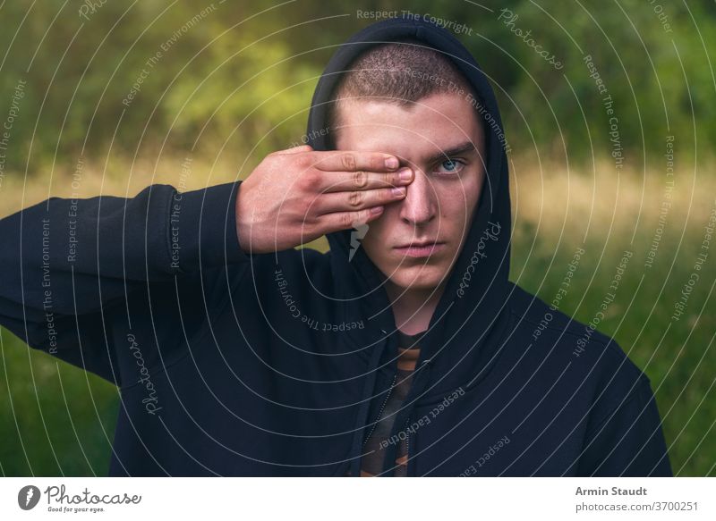 Bildnis eines jungen Mannes mit einem schwarzen Kapuzenpulli, der seine Augen verdeckt Porträt ernst deckend Hand Finger Aussehen Teenager Blick männlich schön