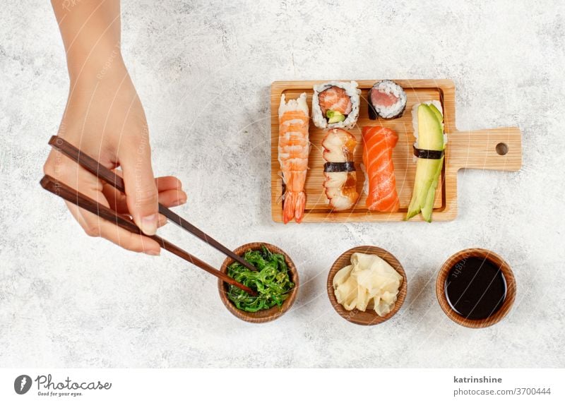 Draufsicht auf die Hand, die eine Rolle mit Stäbchen von einem Teller nimmt Sushi unter Essstäbchen verzehrfertig Essen Sashimi Brötchen Sushi-Bar Esszimmer