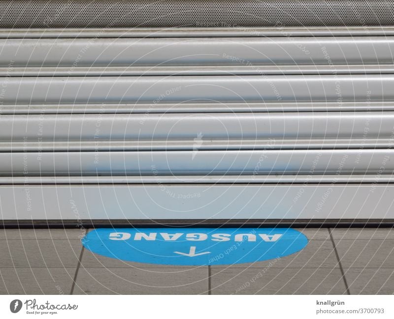 Blauer Aufkleber mit weißer Schrift „AUSGANG“ und weißem Pfeil auf dem Boden vor einem geschlossenen Geschäft Ausgang Schilder & Markierungen Hinweisschild