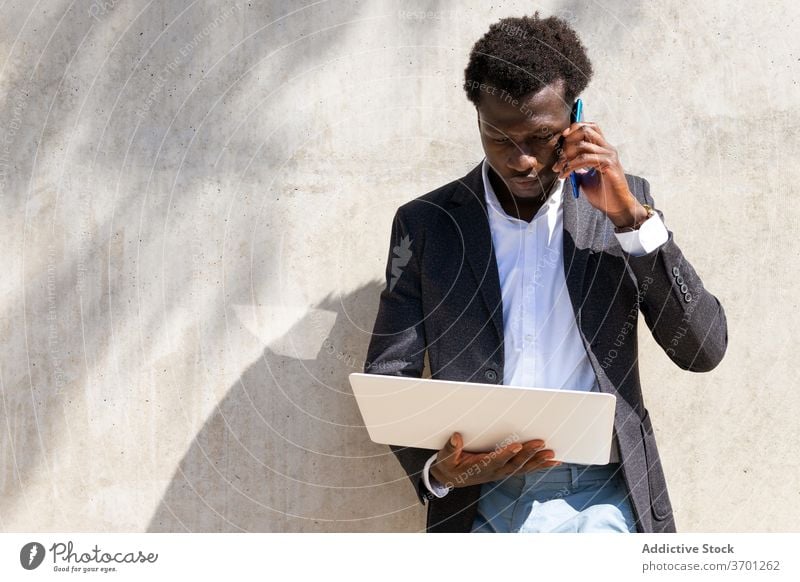Seriöser Geschäftsmann spricht am Handy in der Stadt diskutieren Arbeit Smartphone reden Manager Exekutive Laptop benutzend Business männlich ethnisch schwarz
