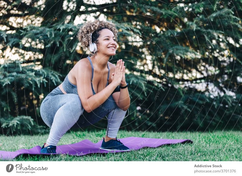Energetische junge Frau Training im Park Fitness Übung Kniebeuge sportlich heiter Energie Kopfhörer Gesundheit Sportbekleidung Wellness passen ethnisch