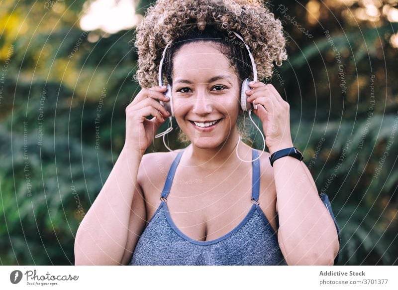 Fröhliche Sportlerin beim Musikhören mit Kopfhörern im Park Frau sportlich zuhören Glück heiter Fitness genießen ausrichten Energie jung Smartphone Training