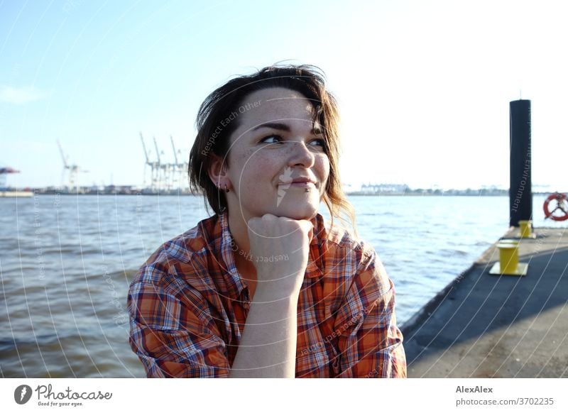 Junge Frau mit Sommersprossen sitzt auf einem Ponton vor Hamburger Hafen Porträt Zentralperspektive Blick brünettes Haar Textfreiraum rechts sommersprossig