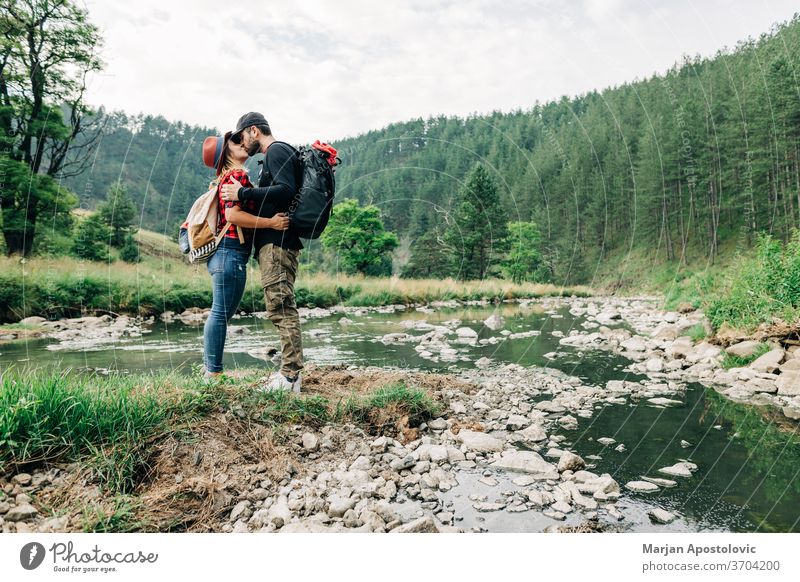 Junges Naturforscherpaar küsst sich in den Bergen am Fluss Erwachsener Abenteuer Rucksack Backpacker lässig Paar Bach Expedition Erkundung erkunden Wald Glück