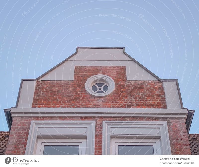 Hausgiebel / Staffelgiebel mit roten Klinkersteinen, weißem Putz und einem runden hübschen Fenster vor hellblauem Himmel Dachgiebel Giebel Backsteine
