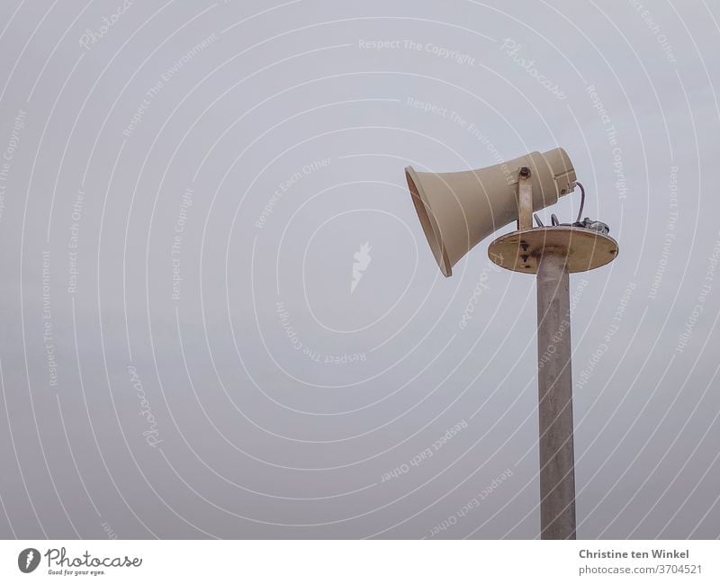 Seitenansicht eines älteren Lautsprechers in Form eines Megaphons vor diesigem Himmel Megafon Mast Kommunizieren Durchsage Information Hintergrund neutral grau
