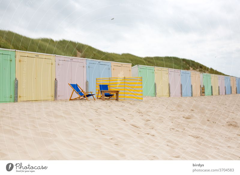 pastellfarbene Strandhütten in einer langen Reihe. 2 leere Liegestühle und ein Windschutz davor Sand Pastellton bunt mehrfarbig Nordseestrand Dünen